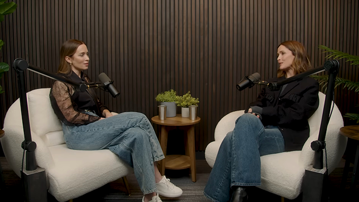 Emily Blunt in a podcast setting, discussing plastic surgery rumors with a female host in a modern studio.