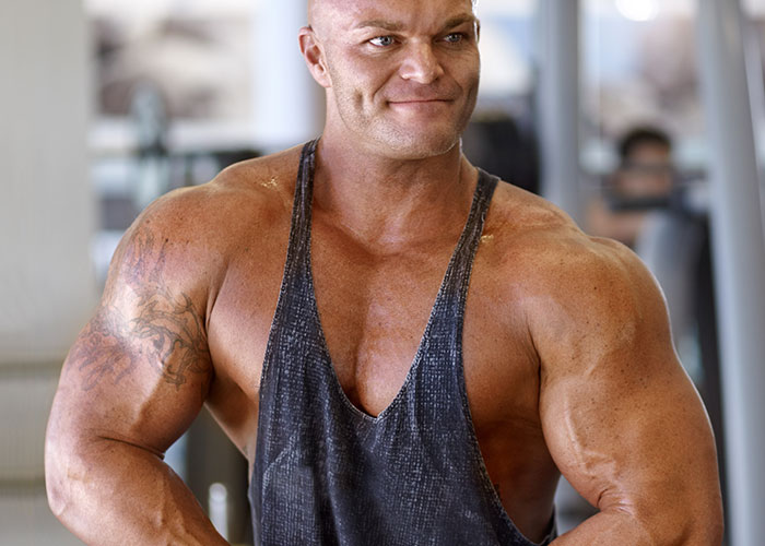 Muscular man in a gym wearing a tank top, representing strength and tension related to risking future child’s health.