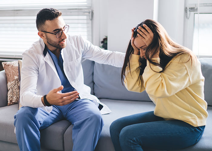 Worried woman holding head as man in white coat talks, depicting conflict over future child’s health risk and exposed lie. Worried woman holding head as man in white coat talks, depicting conflict over future child’s health risk and exposed lie.