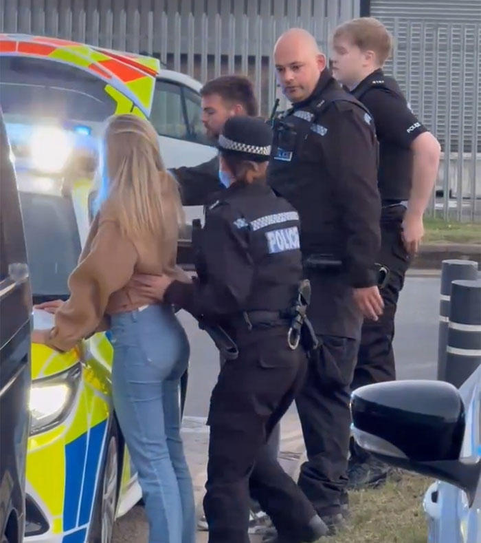 Police officers detaining a young woman beside a patrol car, related to snitch reporting and Bonnie Blue arrest. Police officers detaining a young woman beside a patrol car, related to snitch reporting and Bonnie Blue arrest.