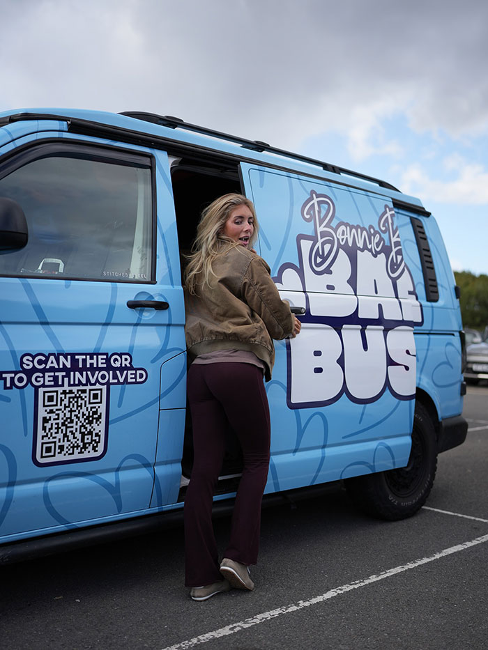 Woman opening door of a blue Bonnie Blue Bus with a QR code to get involved on a cloudy day in a parking lot Woman opening door of a blue Bonnie Blue Bus with a QR code to get involved on a cloudy day in a parking lot