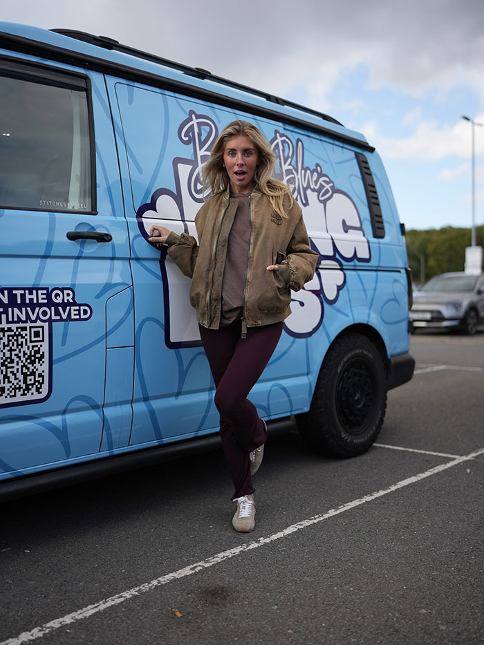 Woman standing defiantly beside a blue van displaying Bonnie Blue's message amid scandalous video controversy. Woman standing defiantly beside a blue van displaying Bonnie Blue's message amid scandalous video controversy.
