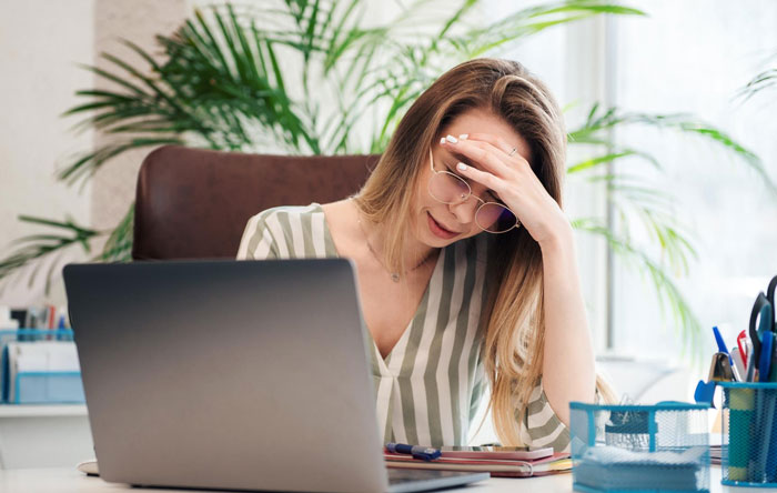 Woman stressed at desk with laptop, reflecting on boss asking to host family and dog for a week without a raise. Woman stressed at desk with laptop, reflecting on boss asking to host family and dog for a week without a raise.