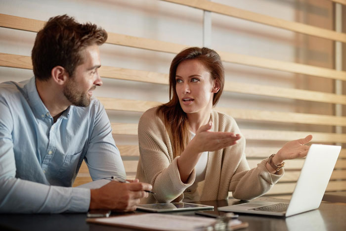 A man and woman in casual clothes discussing work at a table with laptop and tablet, illustrating boss asking lady to host family. A man and woman in casual clothes discussing work at a table with laptop and tablet, illustrating boss asking lady to host family.