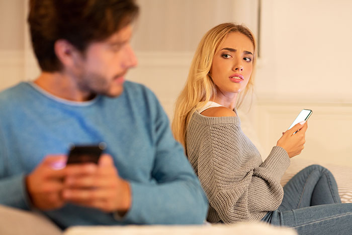 Woman looking upset at boyfriend on phone, highlighting cheating and astrology obsession with Cancer zodiac sign reference.