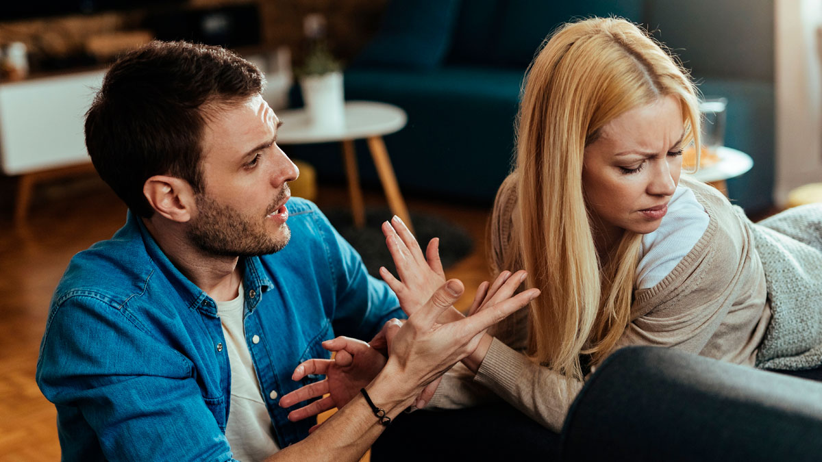 Couple having a tense argument in a living room, woman upset while man explains, relating to astrology and Cancer sign.