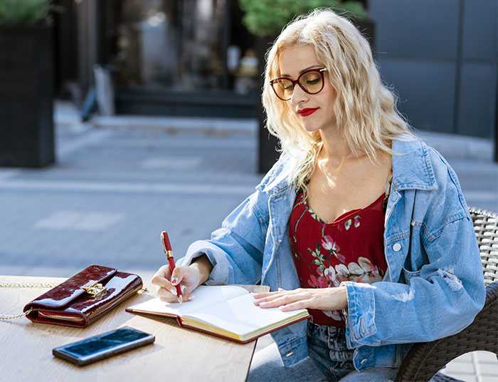 Woman writing novel outdoors, wearing glasses and denim jacket, seeking advice after boyfriend calls the police over her writing. Woman writing novel outdoors, wearing glasses and denim jacket, seeking advice after boyfriend calls the police over her writing.