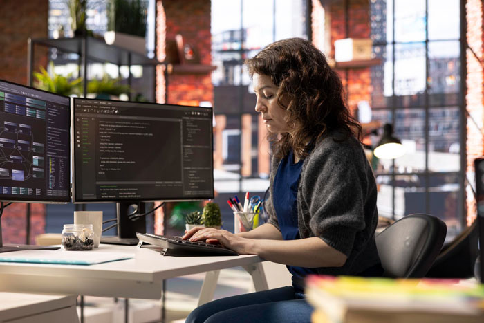 Woman at modern office desk working on computer, appearing focused amid themes of misogyny and jealous girlfriend discomfort.