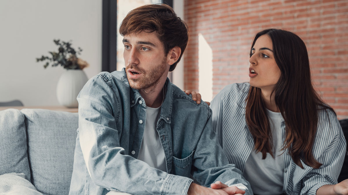 Young man looking worried as his girlfriend pressures him to lie about his career during a tense relationship discussion.