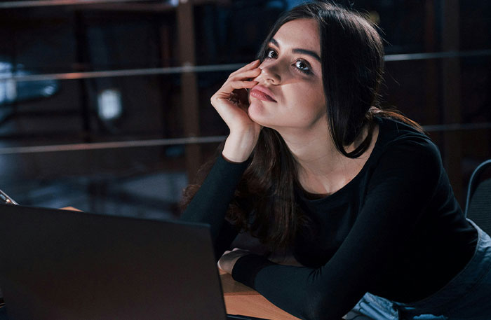 Young woman looking thoughtful while sitting at a desk with a laptop, reflecting on playing video games to unwind. Young woman looking thoughtful while sitting at a desk with a laptop, reflecting on playing video games to unwind.