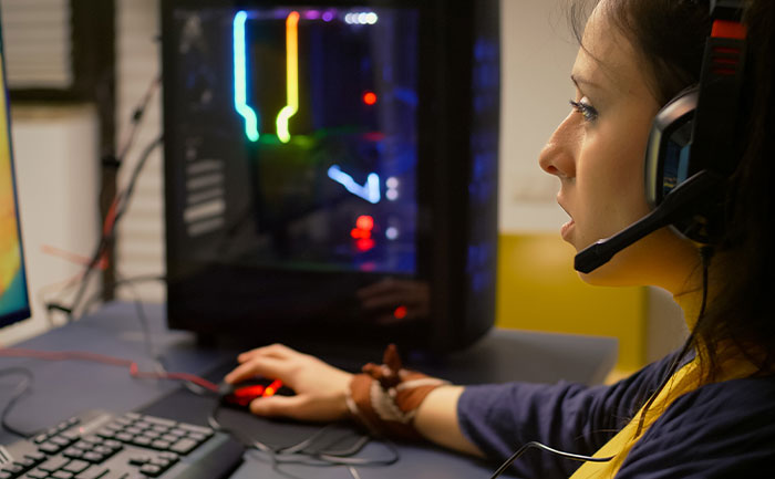 Young woman wearing headphones, focused on playing video games to unwind while seated at a gaming PC setup. Young woman wearing headphones, focused on playing video games to unwind while seated at a gaming PC setup.