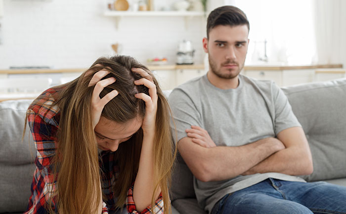 A frustrated couple sitting on a couch, guy mocking girlfriend for playing video games to unwind and saying it isn’t ladylike. A frustrated couple sitting on a couch, guy mocking girlfriend for playing video games to unwind and saying it isn’t ladylike.