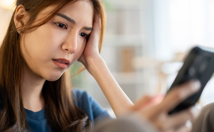 Young woman looking concerned while holding a smartphone, reflecting on a guy mocking girlfriend for playing video games. Young woman looking concerned while holding a smartphone, reflecting on a guy mocking girlfriend for playing video games.