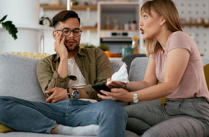 Couple having a tense conversation on couch, guy mocking girlfriend for playing video games to unwind and not being ladylike. Couple having a tense conversation on couch, guy mocking girlfriend for playing video games to unwind and not being ladylike.