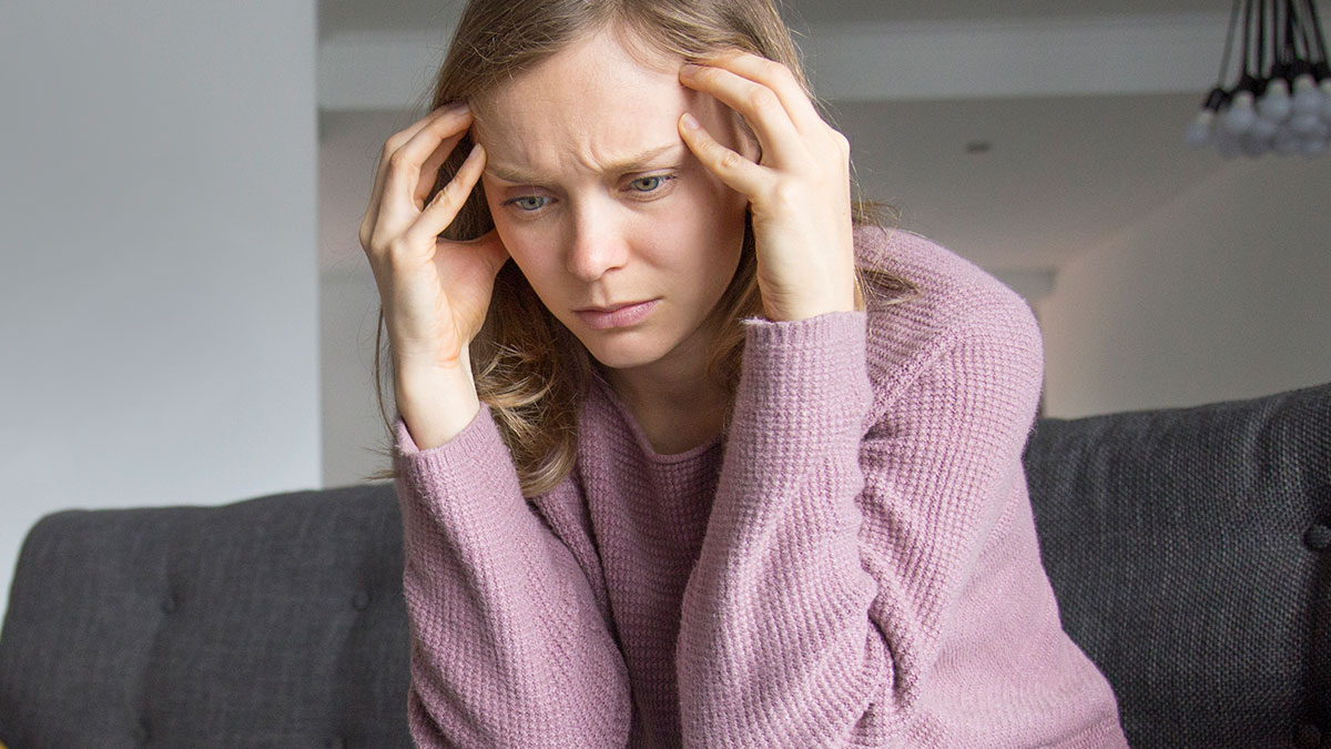 Stressed woman sitting on couch holding her head, reflecting on fiction and IQ shaming in a home setting.