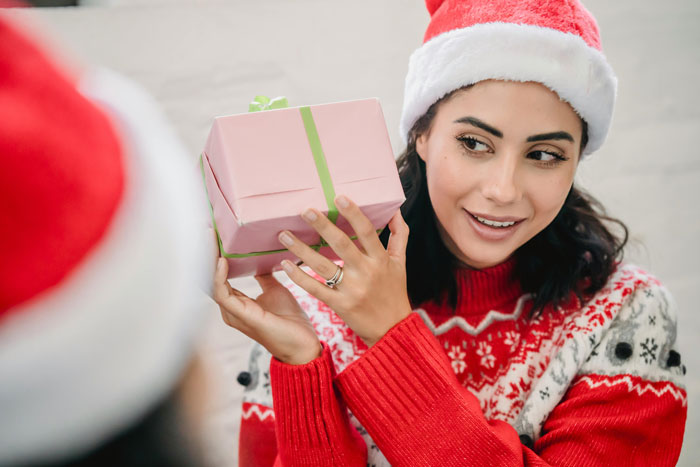 Woman in Santa hat holding pink present, uneasy expression, concept of racist gift and holiday tension Woman in Santa hat holding pink present, uneasy expression, concept of racist gift and holiday tension