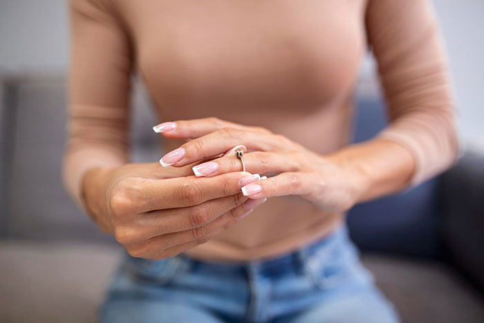 Woman removing engagement ring from finger symbolizing breaking up ultimatum over ring in relationship conflict. Woman removing engagement ring from finger symbolizing breaking up ultimatum over ring in relationship conflict.