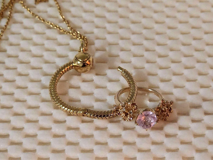 Gold ring with pink stone and matching bracelet on textured white surface, representing breaking up ultimatum over ring.