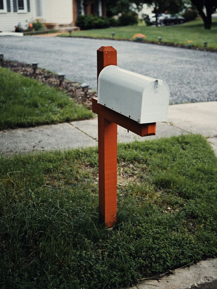 White mailbox on a wooden post surrounded by grass and sidewalk, representing brilliantly sneaky acts of revenge.