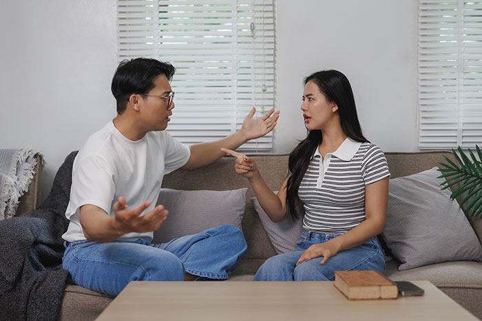 Man and woman having a heated discussion on couch, illustrating conflict from guy giving old laptop to his cat instead of sister.