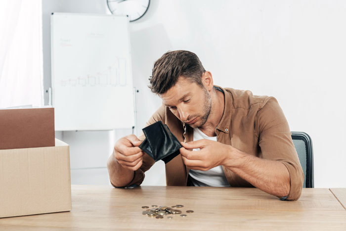 Young man at table holding empty wallet and counting few coins, worried about money Young man at table holding empty wallet and counting few coins, worried about money