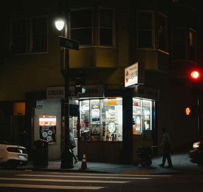 Nighttime view of a liquor store on a city corner with illuminated signs and pedestrians nearby related to raccoon raid. Nighttime view of a liquor store on a city corner with illuminated signs and pedestrians nearby related to raccoon raid.