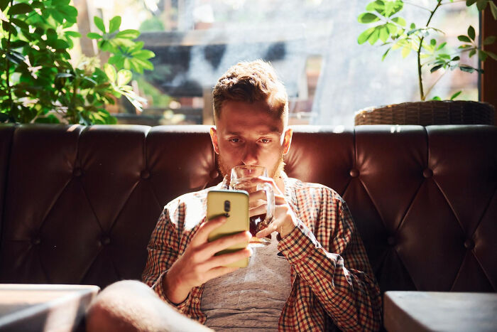 Young man sitting in a cafe, focused on phone while drinking coffee, illustrating small decisions with life-altering consequences.