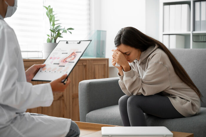 Woman sitting on a couch looking distressed during a medical consultation, illustrating small decisions leading to unexpected consequences.