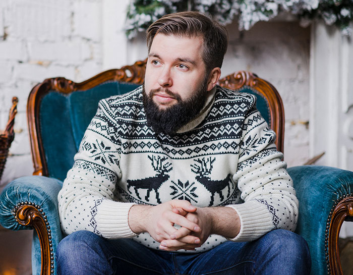 Bearded guy in a patterned sweater sitting thoughtfully in a vintage chair after siblings share surprise plans. Bearded guy in a patterned sweater sitting thoughtfully in a vintage chair after siblings share surprise plans.