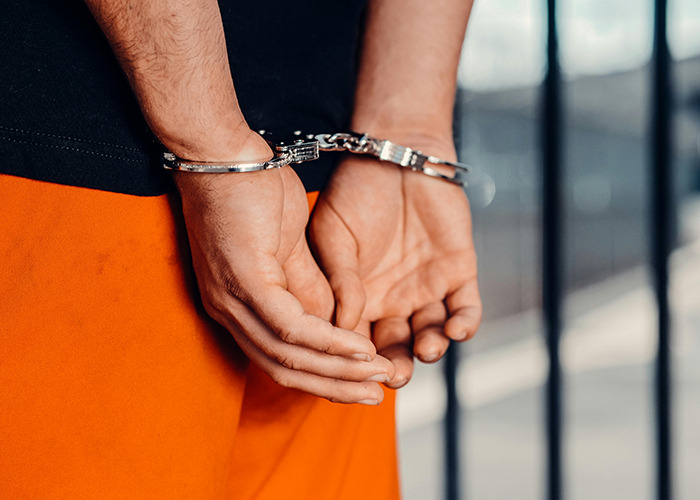 Hands of a person in handcuffs wearing orange pants, symbolizing arrest of a terrible psychopath caught on CCTV footage. Hands of a person in handcuffs wearing orange pants, symbolizing arrest of a terrible psychopath caught on CCTV footage.