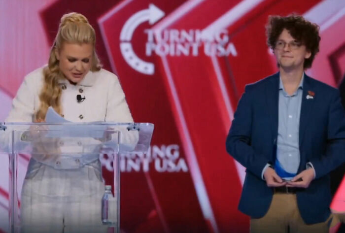 Erika Kirk making an awkward Freudian slip at a Turning Point USA event, standing beside a young man on stage. Erika Kirk making an awkward Freudian slip at a Turning Point USA event, standing beside a young man on stage.