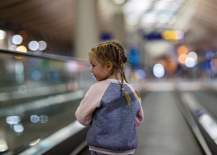 Young girl with braided hair on an airport moving walkway amid a chaotic scene with blurred lights and people in the background