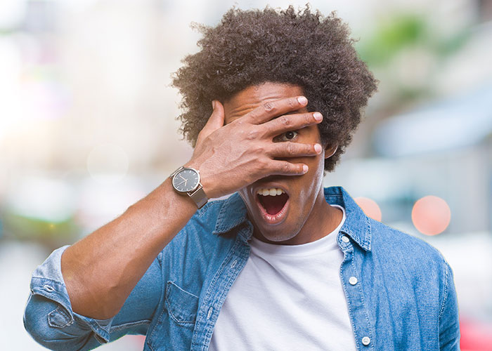 Man in denim shirt showing shock and surprise, capturing a chaotic scene witnessed firsthand outdoors.
