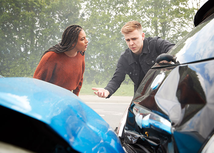 Two people inspecting chaotic car accident damage during a stressful scene witnessed outdoors by many.