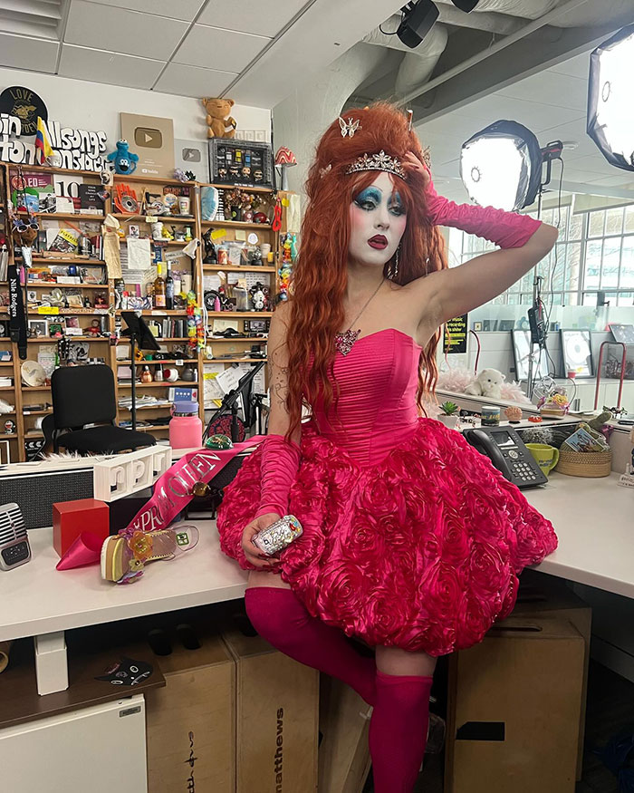 Chappell Roan in a pink dress and dramatic makeup, posing amid studio equipment and awards, facing Brigitte Bardot backlash.
