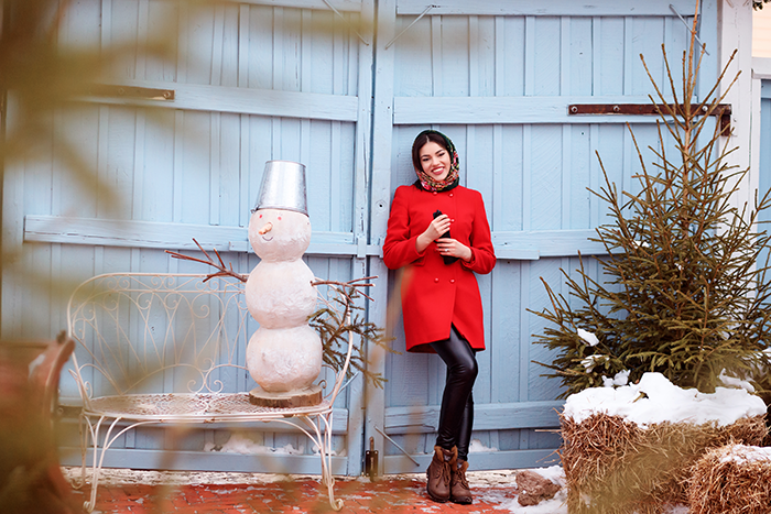 Woman standing next to festive Christmas decor outside, facing HOA fine for decorations deemed too excessive this holiday season