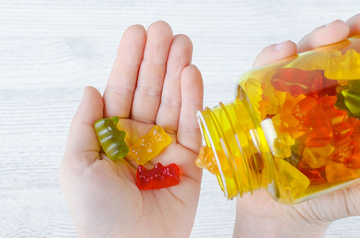 Hand holding colorful gummies poured from a yellow bottle, illustrating mom calls 911 after kids eat her gummies controversy. Hand holding colorful gummies poured from a yellow bottle, illustrating mom calls 911 after kids eat her gummies controversy.