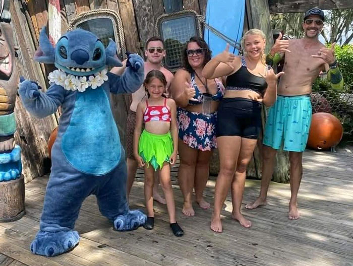 Family posing with Stitch character at theme park, smiling and making hand gestures, reflecting a Christmas gift haul for daughter.