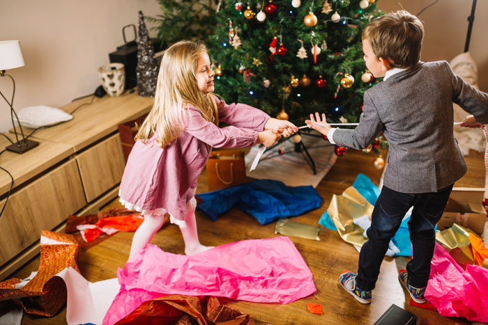 Two unruly children tugging a ribbon near a decorated Christmas tree with torn wrapping paper on the floor. Two unruly children tugging a ribbon near a decorated Christmas tree with torn wrapping paper on the floor.