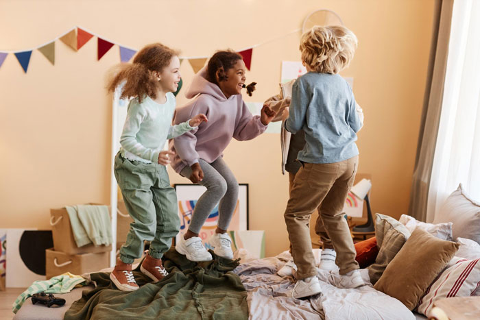Three unruly kids jumping on a bed in a colorful room, illustrating chaos around no Christmas gifts from aunt. Three unruly kids jumping on a bed in a colorful room, illustrating chaos around no Christmas gifts from aunt.