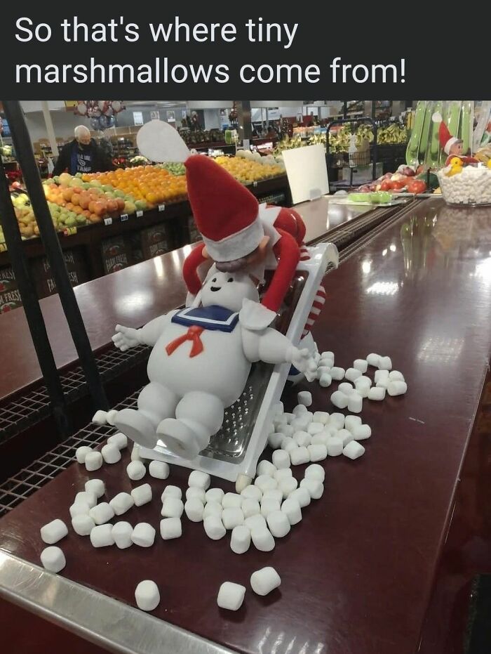 Elf doll grating a Stay Puft Marshmallow Man figure with marshmallows spilled around in a funny Christmas meme scene.