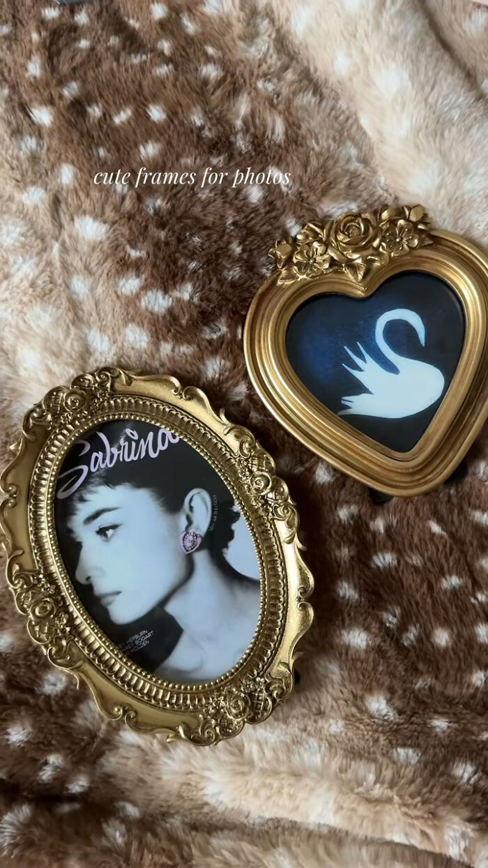 Two ornate gold photo frames, one heart-shaped and one oval, displayed on a soft brown and cream patterned fabric.