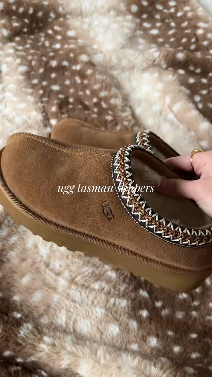 Brown UGG Tasman slippers with cozy lining held over a soft brown and white patterned blanket as a Christmas gift idea.