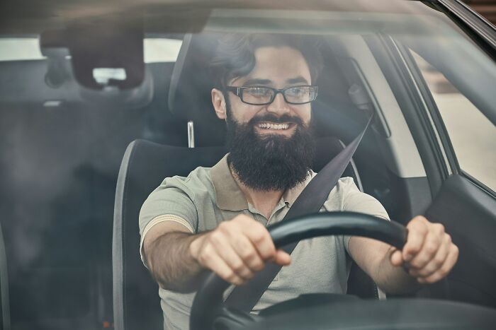 Bearded man smiling behind the wheel, driving home after one of the wildest work Christmas parties ever.