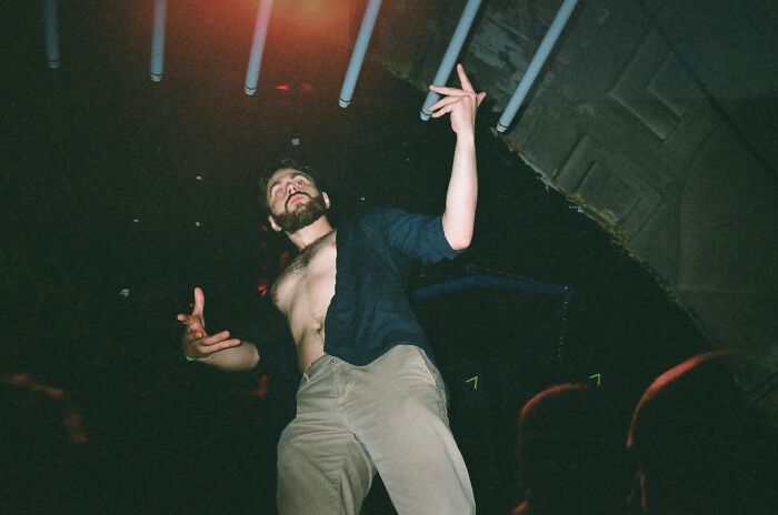 Man partying wildly at a work Christmas party with shirt open, captured in a low-angle shot during a lively celebration.