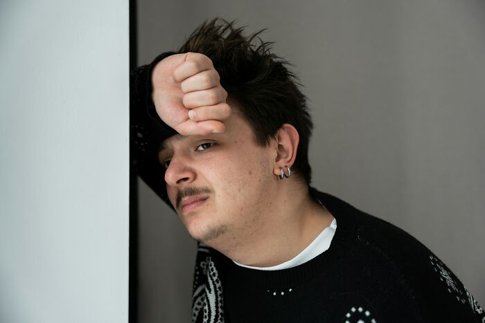 Young man looking exhausted and regretful after a wild work Christmas party, reflecting on the event’s crazy moments.