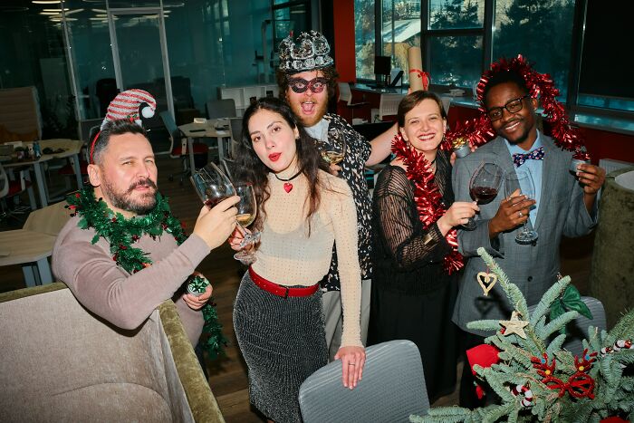 Group of coworkers celebrating with drinks and festive accessories at a work Christmas party turned wild.