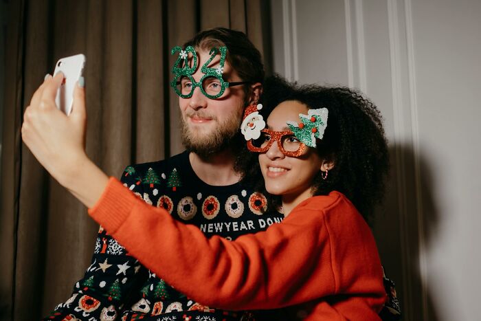 Couple wearing festive glasses at a work Christmas party taking a selfie, capturing wild and fun moments.