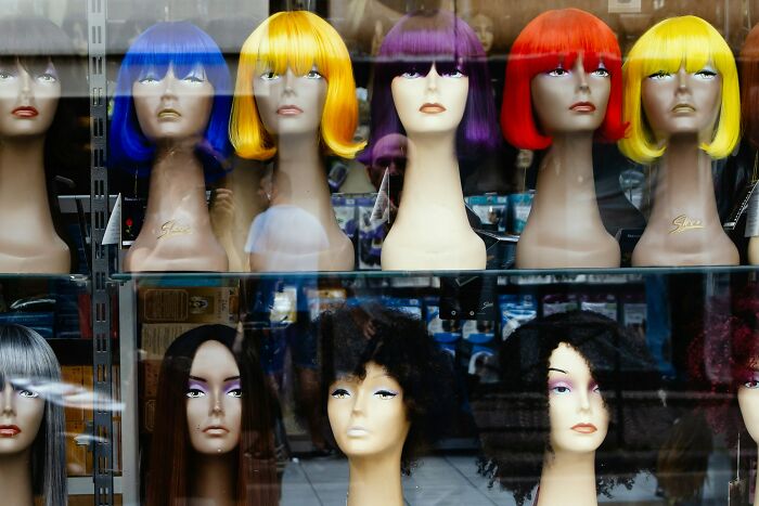 Mannequin heads with colorful wigs displayed in a shop window, symbolizing wild and unexpected work Christmas party stories.