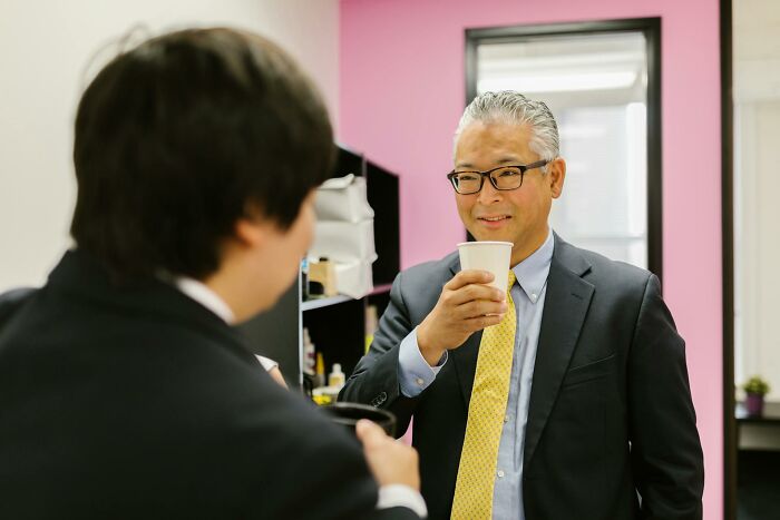 Two coworkers in office attire enjoying drinks and chatting during a work Christmas party atmosphere.